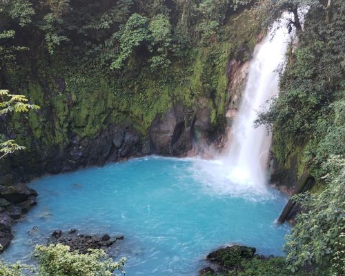 Catarata que da a río con aguas cristalinas color azul claro con vegetación verde alrededor, río Celeste, cerca de La Fortuna.